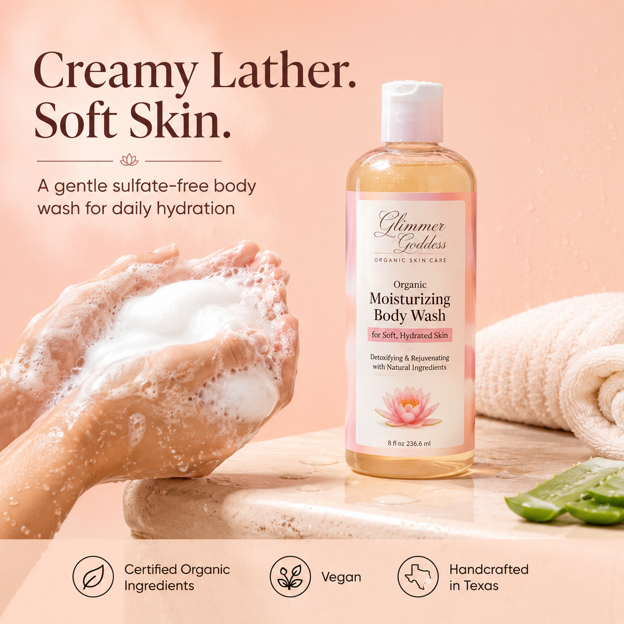 Glimmer Goddess Organic Moisturizing Body Wash lifestyle image on a soft peach background, showing the exact product bottle beside creamy sulfate-free lather in clean wet hands, highlighting soft hydrated skin, Certified Organic Ingredients, vegan body care, and handcrafted in Texas.