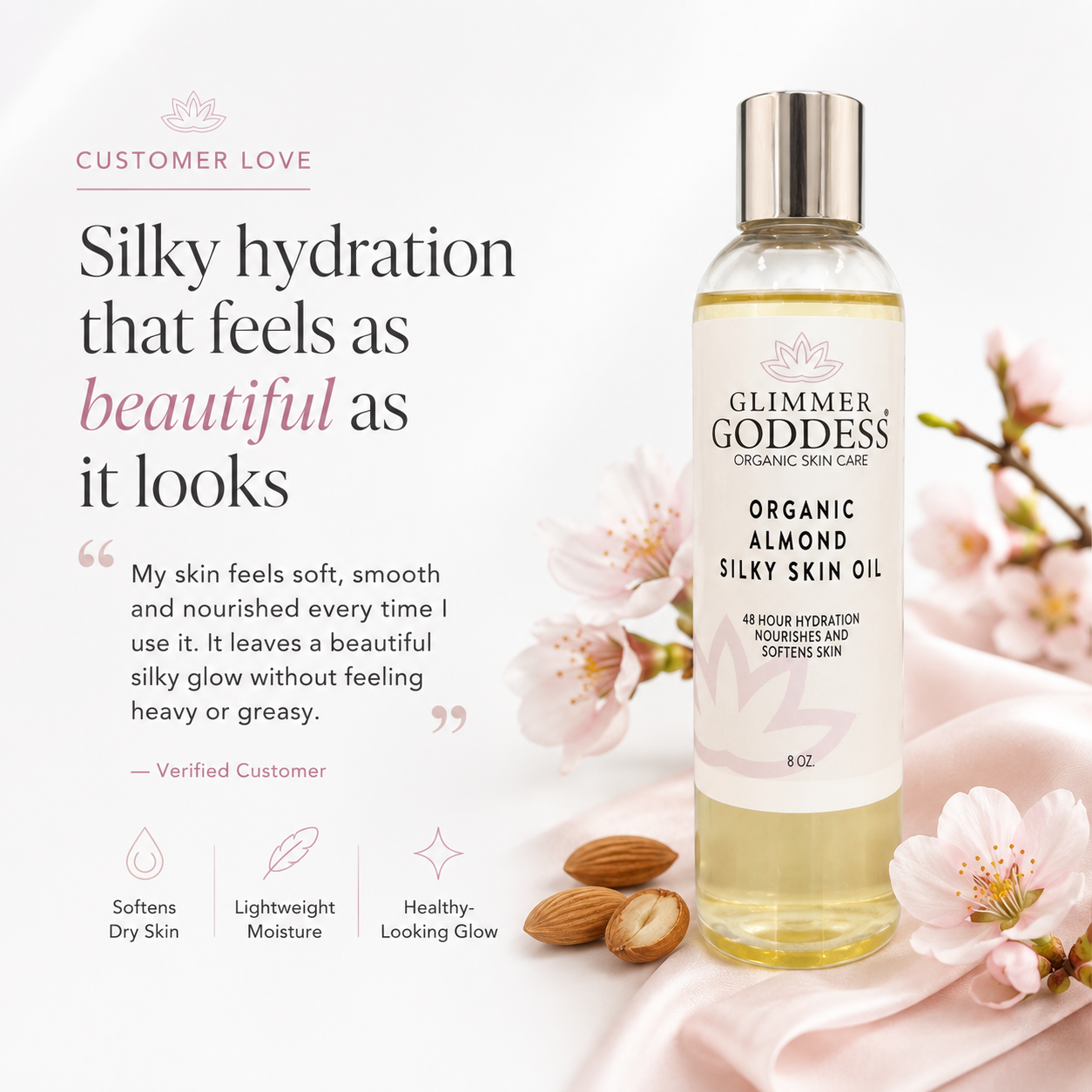 A bottle of Glimmer Goddess Organic Almond Skin Oil stands on pink fabric beside almonds and pink blossoms, with promotional text on the left reading 'Silky hydration that feels as beautiful as it looks.'.