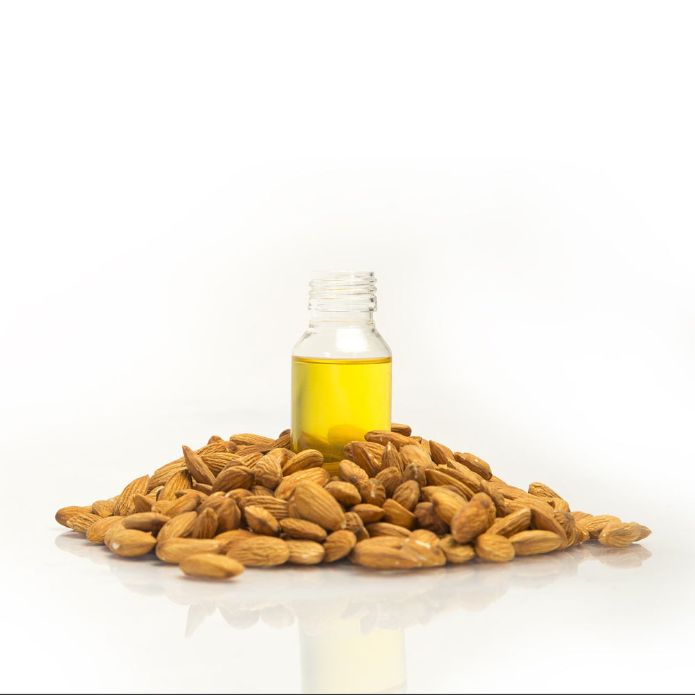Clear bottle of almond oil surrounded by raw almonds on white background
