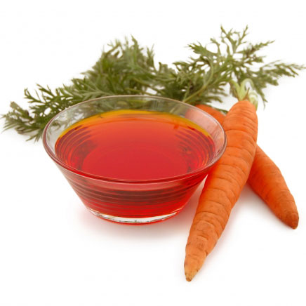 Fresh carrots with green tops and a glass bowl of carrot oil on a white background