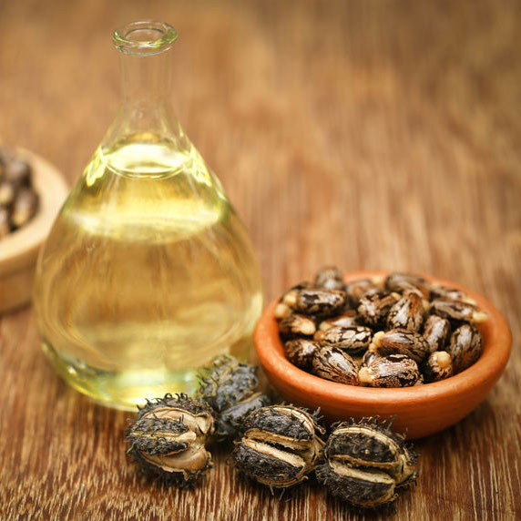 Glass bottle of castor oil with castor seeds in a clay bowl on wooden table