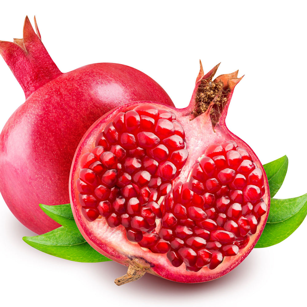 Fresh whole and halved pomegranate with seeds and green leaves on white background